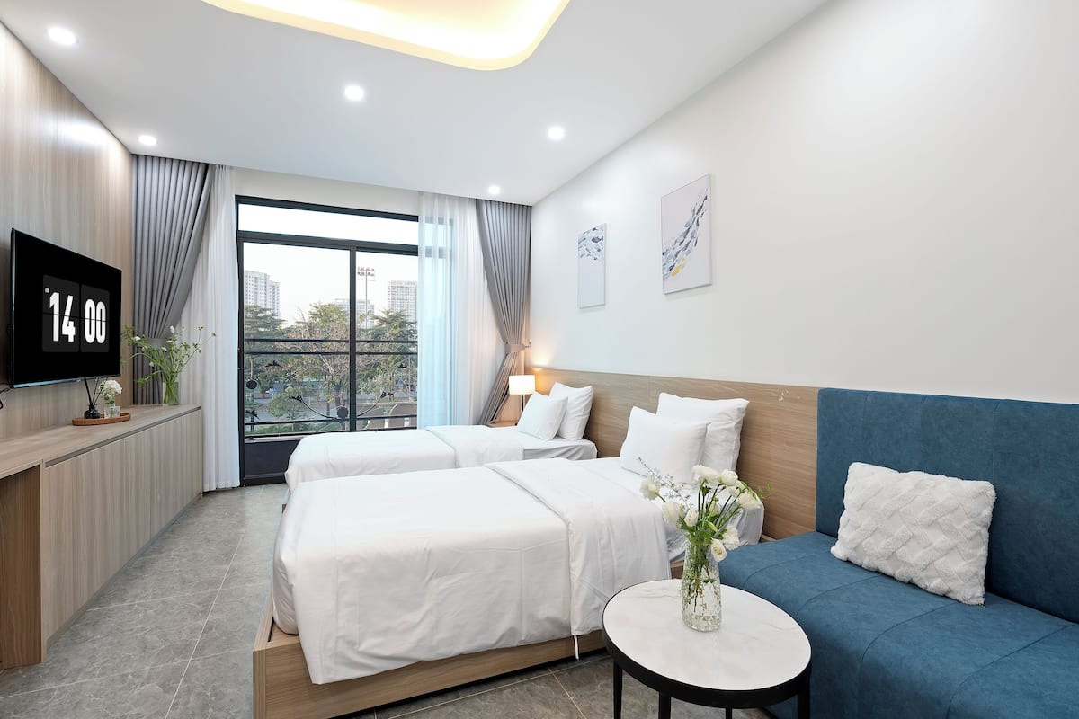A hotel room with two beds, a sofa, a TV, and a window with curtains.