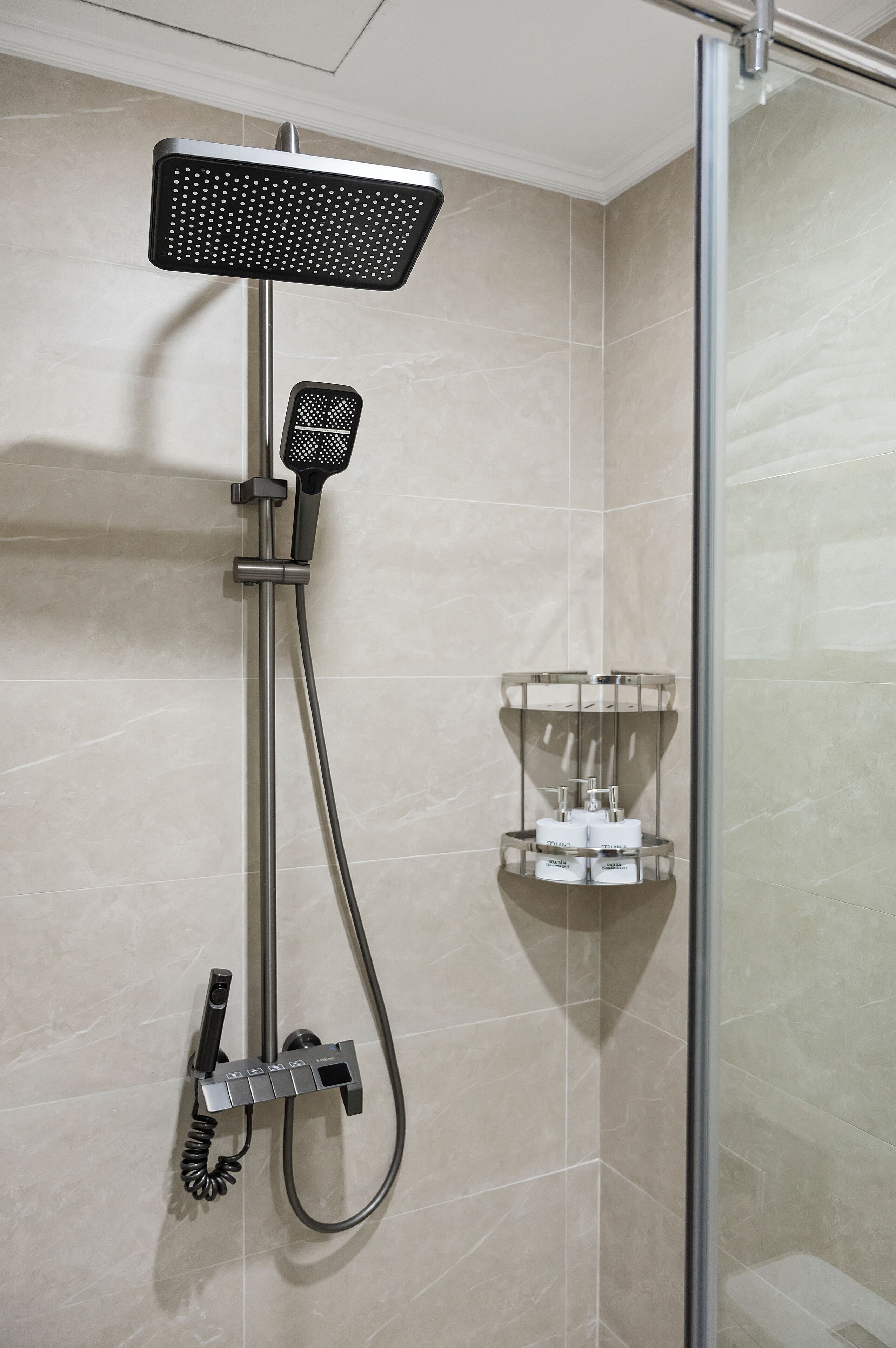 A shower with a handheld showerhead and a wall-mounted panel, a glass shower enclosure, and a shelf with toiletries.