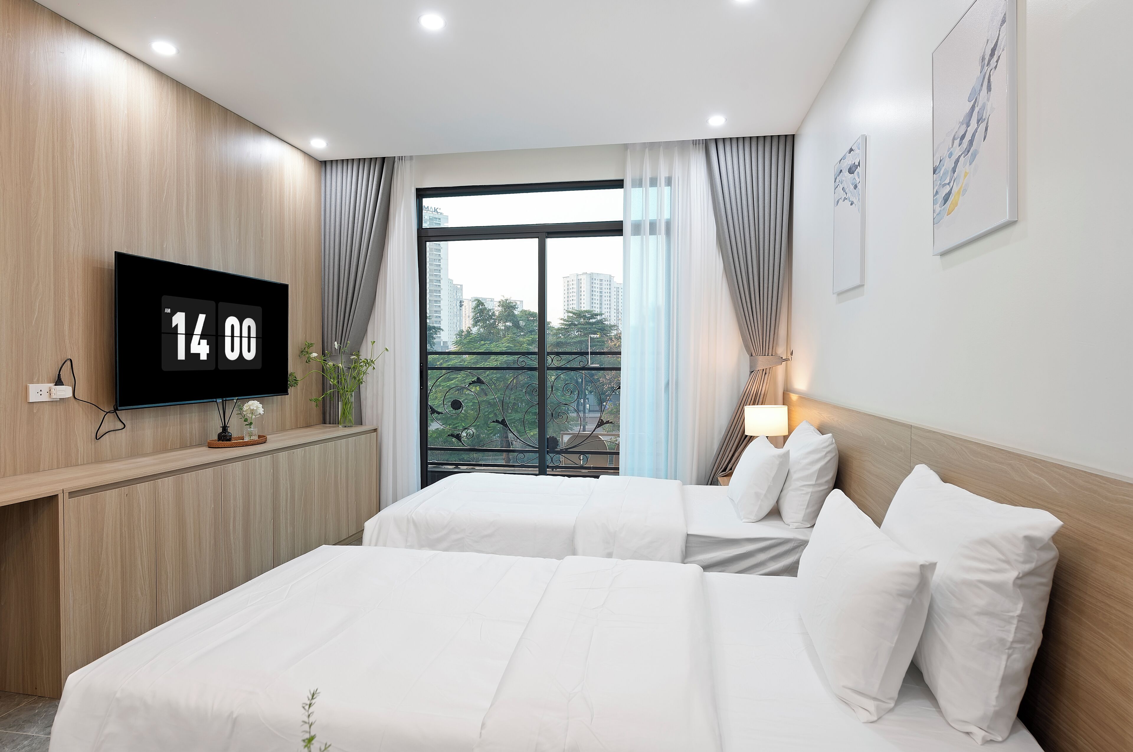 Camera d'albergo con due letti, una televisione, un'ampia finestra con tende e opere d'arte appese al muro.