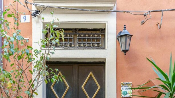 A black door with diamond-shaped gold accents, a number '9' sign, and a small sign above the door. - At Mary's House II (Catania)