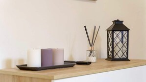 A wooden table with candles, a glass container with reed diffusers, and a black lantern. - At Mary's House II (Catania)