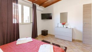 A bedroom with a bed, a dresser, a television, and a window with curtains. - At Mary's House II (Catania)