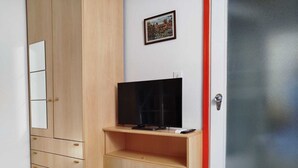 A room with a wooden wardrobe, a television on a wooden shelf, and a door with a frosted glass panel. - Historic apartment on Avenue (Trieste)