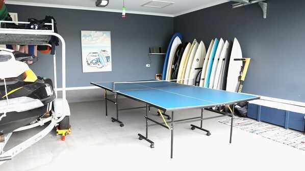 A room with a ping pong table, surfboards, and a toy car.