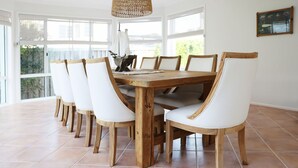 A dining area with a wooden table and white chairs, large windows, and a hanging light fixture.