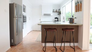 A modern kitchen with a built-in refrigerator, oven, and microwave, a wooden island with bar stools, and a view of greenery outside.