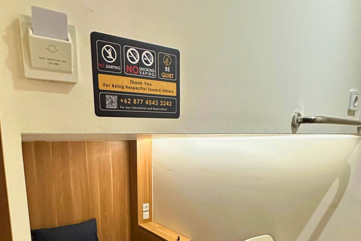 A compact room with a bunk bed, a desk, and a chair. There is a sign with rules and a QR code.