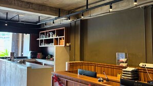 A reception desk with a wooden finish, a computer, and a telephone. There are shelves with various items and a window providing natural light. - ALTHIA PRIVATE CAPSULE QUARTERS (Legian)