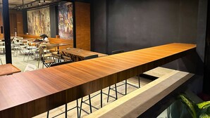 A modern dining area with long wooden tables and chairs, a large abstract painting on the wall, and a concrete ceiling with exposed beams. - ALTHIA PRIVATE CAPSULE QUARTERS (Legian)