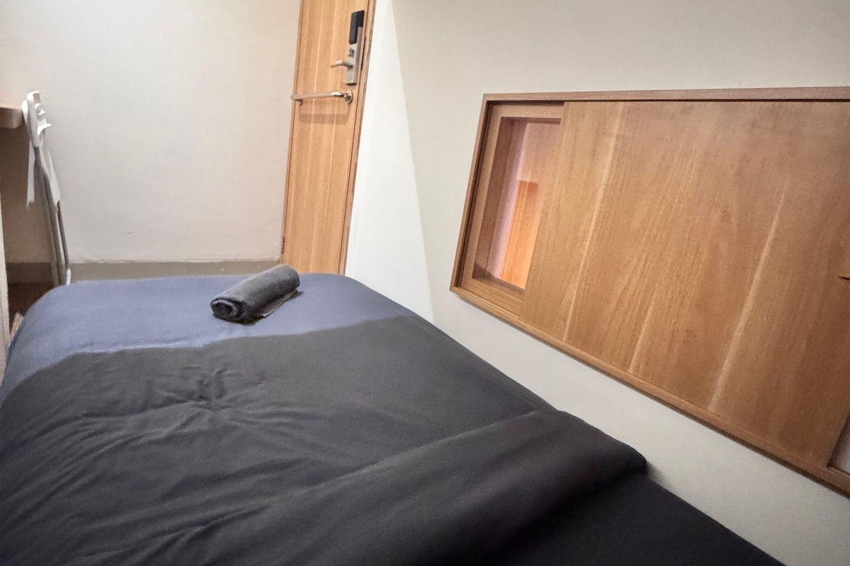 A bedroom with a bed, a wooden wardrobe, a window, and a door.