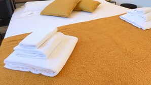 A hotel room with a bed, two pillows, and two folded towels on a brown carpet.
