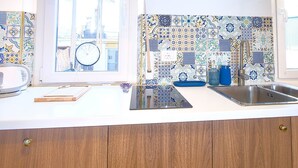 A kitchen with a white countertop, a sink, a clock, and a window with a view of buildings.