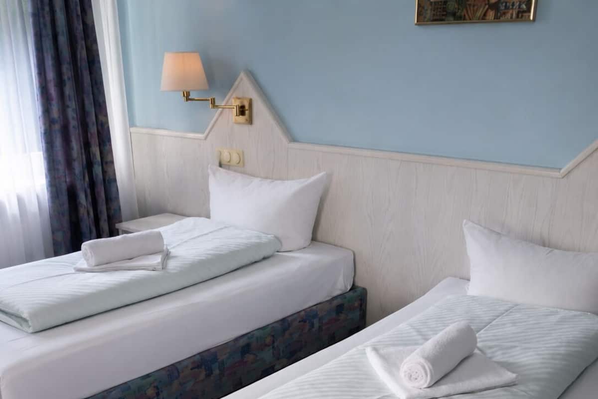 Habitación de hotel con dos camas, una mesita de noche, una lámpara y un cuadro en la pared.