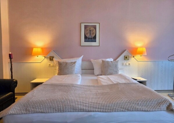 Une chambre d’hôtel avec un grand lit, deux lampes de chevet, un tableau encadré au mur et une chaise noire.