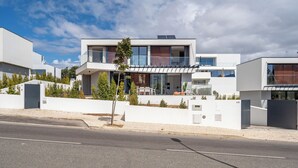 A modern two-story house with a balcony, a driveway, and a small garden.
