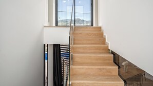 A modern staircase with wooden steps and glass railings, leading to a room with a large window offering a view of the outdoors.