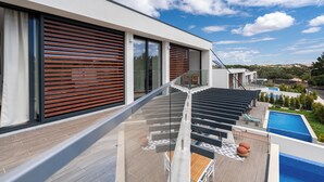 A modern building with large windows, a balcony with a glass railing, and a pool area.