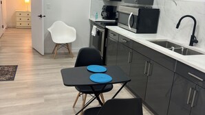 A modern kitchen with dark cabinets, a black countertop, and a stainless steel sink. There is a small dining area with two black chairs and a table. - Cozy, 2BR apt., fully furnished! (Edmonton)