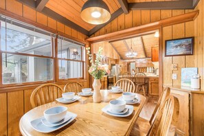 A wooden dining area with a table set for six, surrounded by wooden chairs. A vase with flowers is placed on the table. - Stay In Lakeside - Lake Front Oasis (Lakeside)