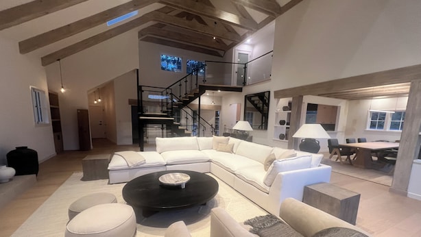 Un vaste espace de vie comprenant un grand canapé d’angle, une table basse ronde et un escalier menant à un niveau supérieur.