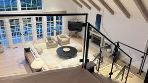 Un vaste espace de vie doté d’un haut plafond, de grandes fenêtres et d’un escalier menant à l’étage supérieur.