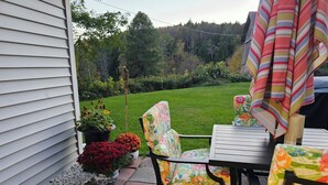 Une terrasse avec une table et des chaises, des plantes en pot et une vue sur une cour verdoyante.