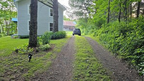 Une allée de gravier mène à une maison bleu clair, entourée de verdure.