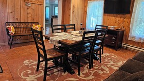 Une pièce aux murs lambrés, avec une table à manger dressée pour quatre personnes, un banc agrémenté de coussins, un téléviseur fixé au mur et un tapis à motifs.