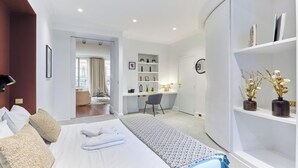 A modern hotel room with a neatly made bed, a desk, and a bookshelf.