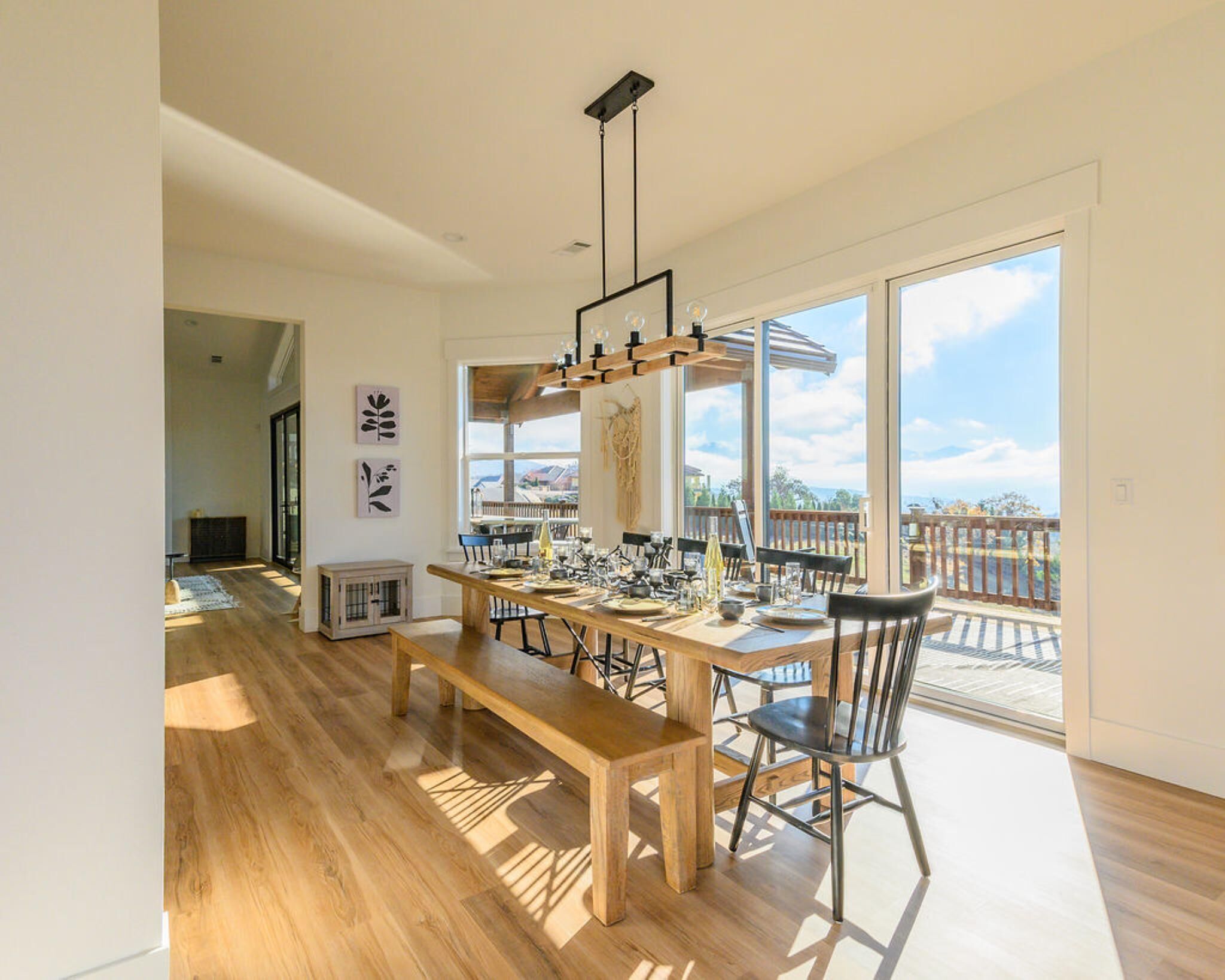 Un comedor amplio con una mesa de madera y bancos, ventanas grandes que ofrecen vistas al exterior y una lámpara colgante moderna.