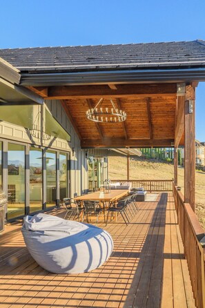 Een terras buiten met een houten tafel en stoelen, een hanglamp en een grote relaxfauteuil.