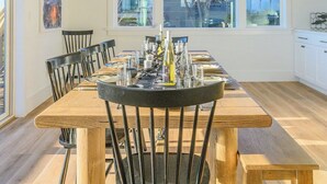 Un comedor moderno con una mesa y sillas de madera, una lámpara colgante y ventanas amplias con vistas al exterior.
