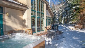 Un bain à remous installé dans un espace extérieur enneigé, avec un mur en pierre et une terrasse en bois.