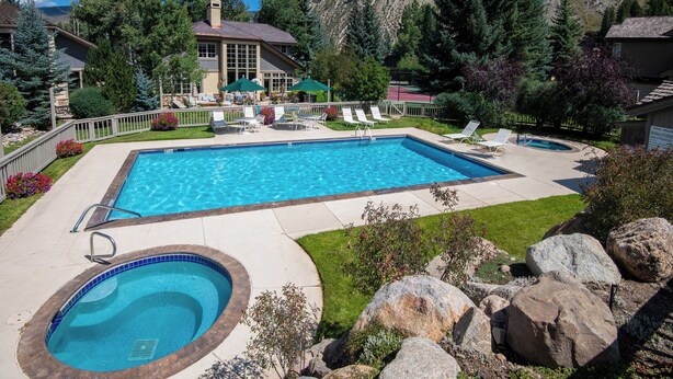 Une piscine rectangulaire avec un jacuzzi, entourée d’une terrasse dotée de chaises longues et d’un petit jardin.
