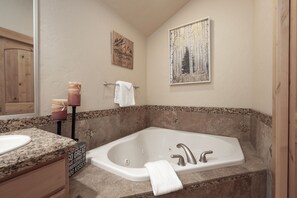Une salle de bain dotée d’une grande baignoire, d’un lavabo avec un plan de travail en granit et d’un meuble en bois.