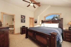 Une chambre à coucher avec un lit en bois, un ventilateur de plafond, une commode en bois et une vue sur les arbres par la fenêtre.