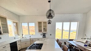 Una cocina moderna con una isla grande, paredes de ladrillo blanco y vistas a un campo a través de amplios ventanales.