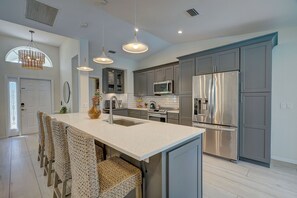 Una cocina moderna con gabinetes grises, electrodomésticos de acero inoxidable y una isla central con taburetes de bar.