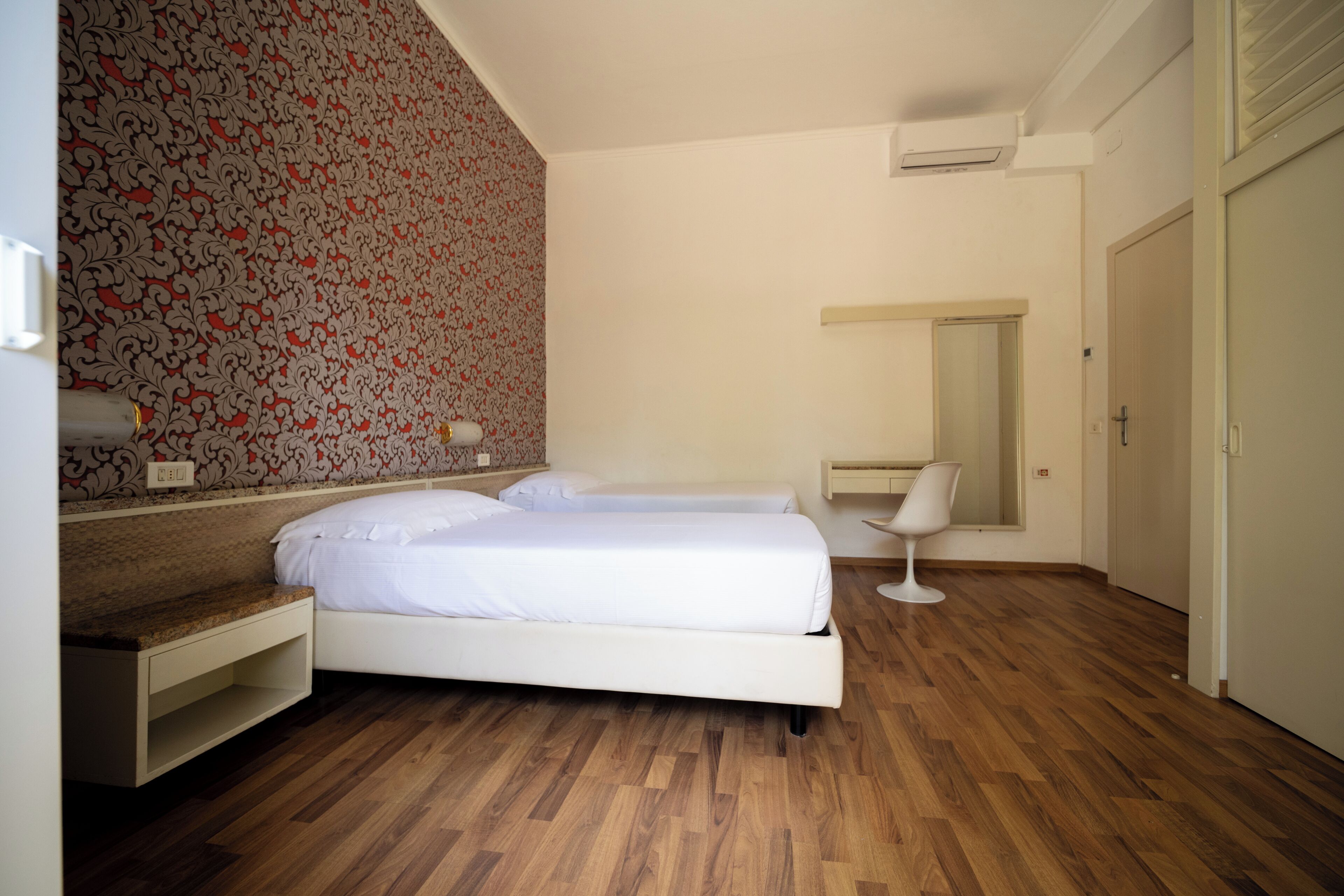 A bedroom with a bed, a bedside table, a chair, and a mirror.