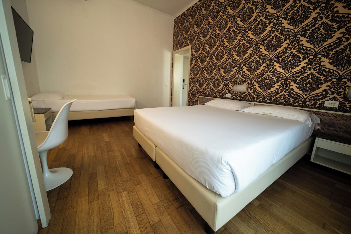 A bedroom with a large bed, a smaller bed, a chair, and a patterned wall.