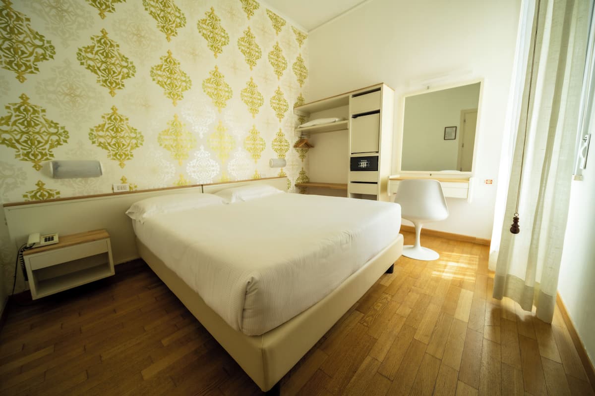 A bedroom with a large bed, a bedside table, a wardrobe, a mirror, and a bathroom with a sink and toilet.