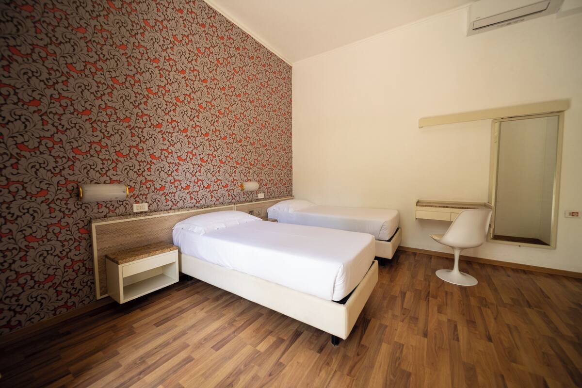 A bedroom with two beds, a bedside table, a chair, and a mirror.