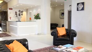 A modern hotel lobby with a reception desk, black leather sofas, and a glass coffee table with magazines. - Hotel Rosabianca (Rimini)