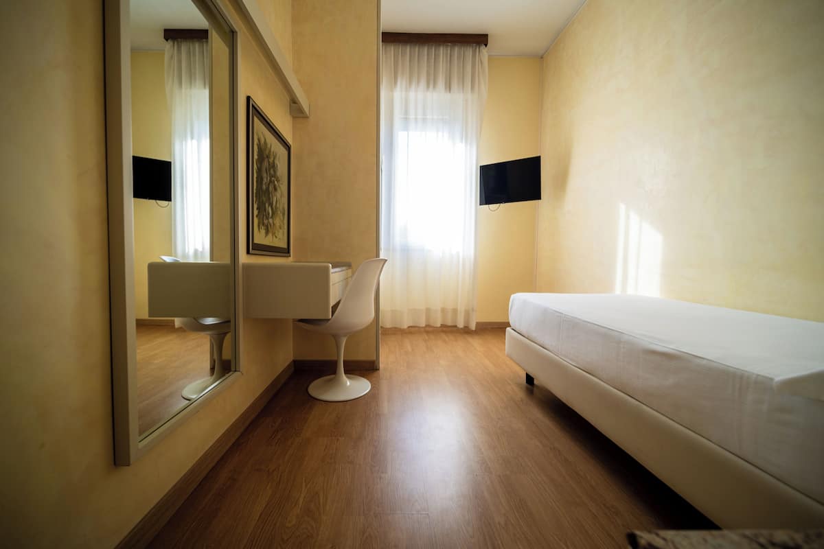 A hotel room with a bed, a chair, a desk, a mirror, and a television.