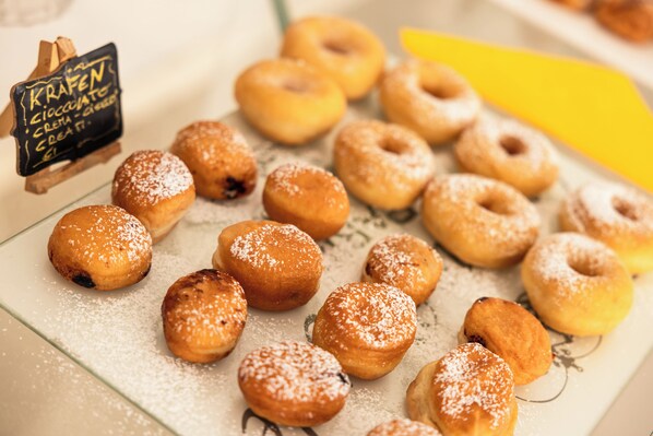 A variety of donuts on a tray, some dusted with powdered sugar. - Hotel Rosabianca (Rimini)