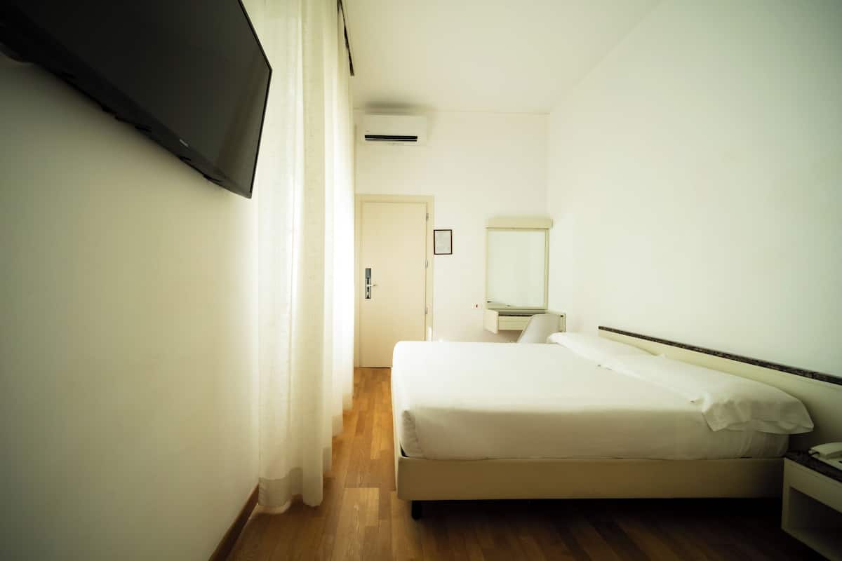 A hotel room with a bed, a bedside table, a mirror, and a TV mounted on the wall.