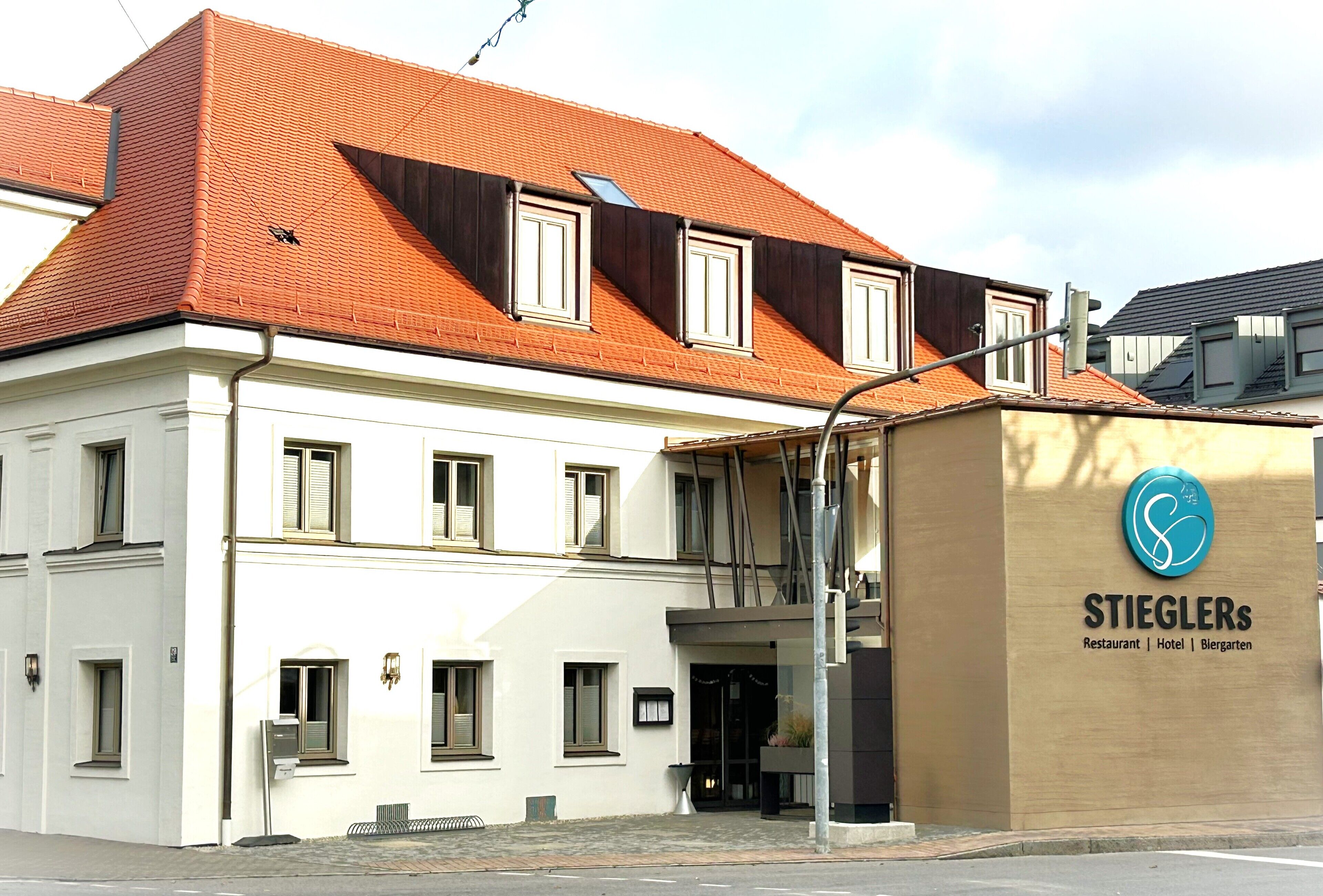 Un bâtiment avec un toit recouvert de tuiles rouges, de nombreuses fenêtres et une enseigne indiquant « Restaurant STIEGLERS | Hôtel | Blergarten ».