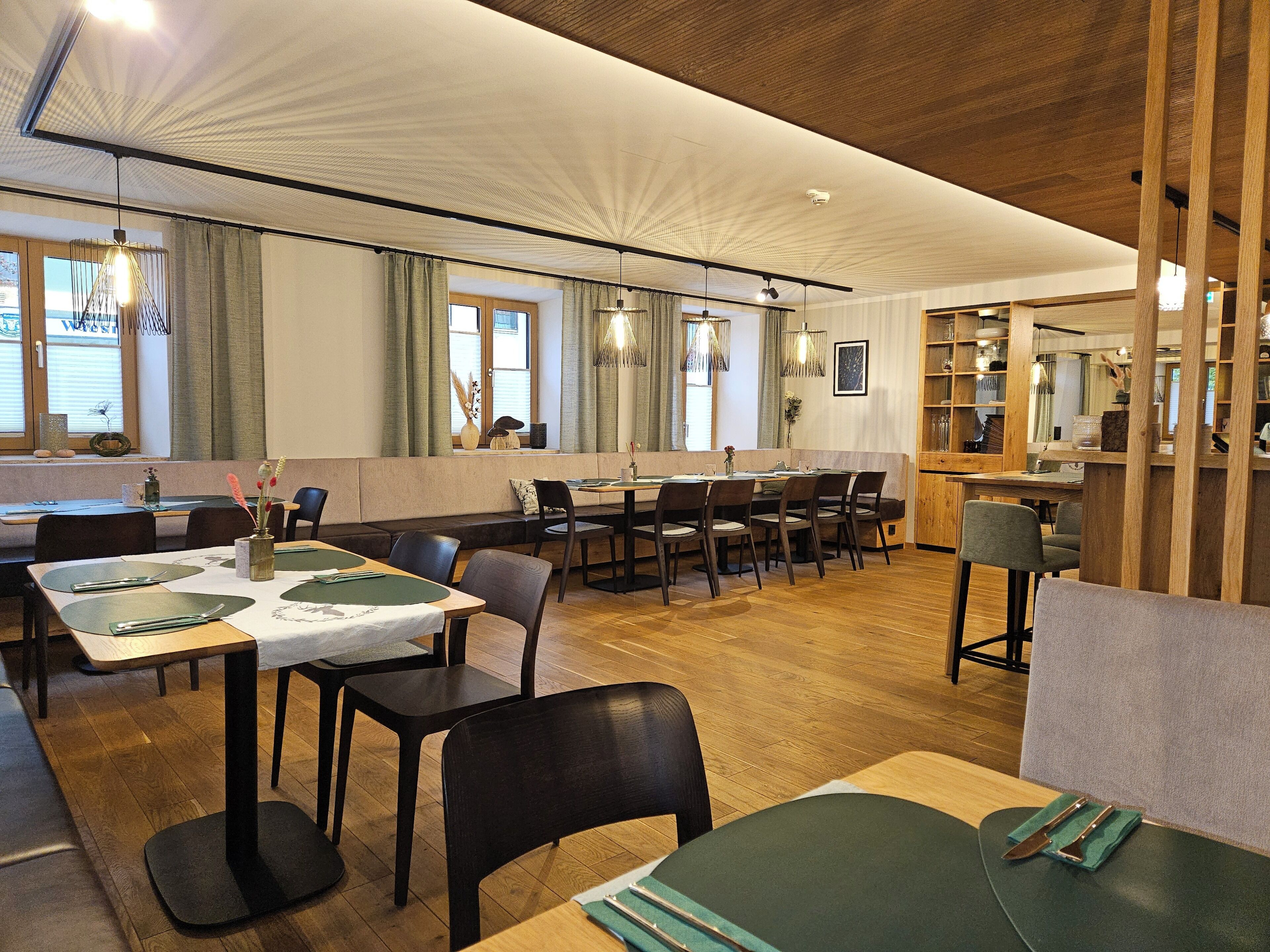 Un restaurant doté d’un plancher en bois, de sièges rembourrés de couleur verte et d’un éclairage suspendu.
