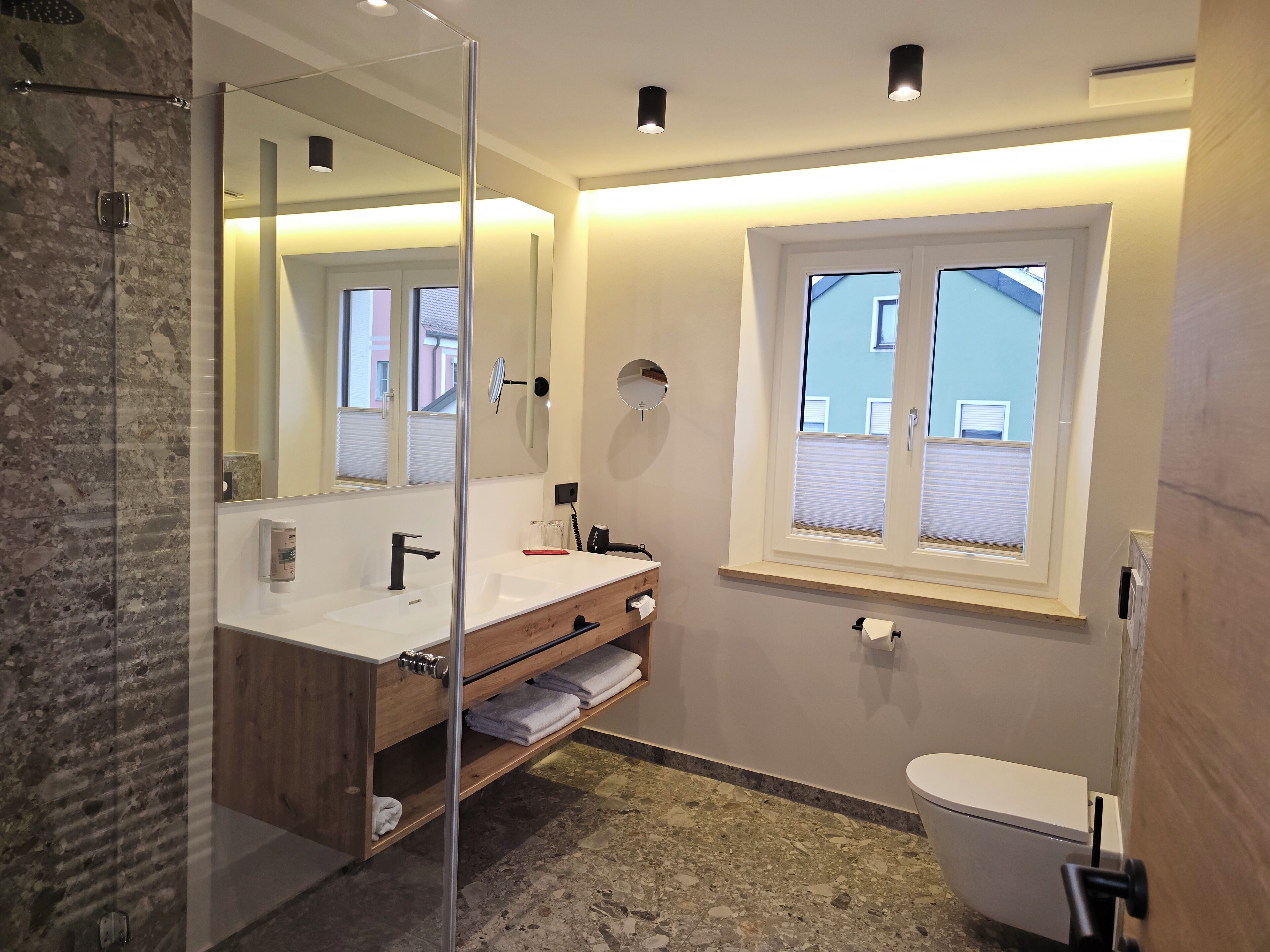A modern bathroom with a glass shower enclosure, a wooden vanity, a white sink, and a toilet.