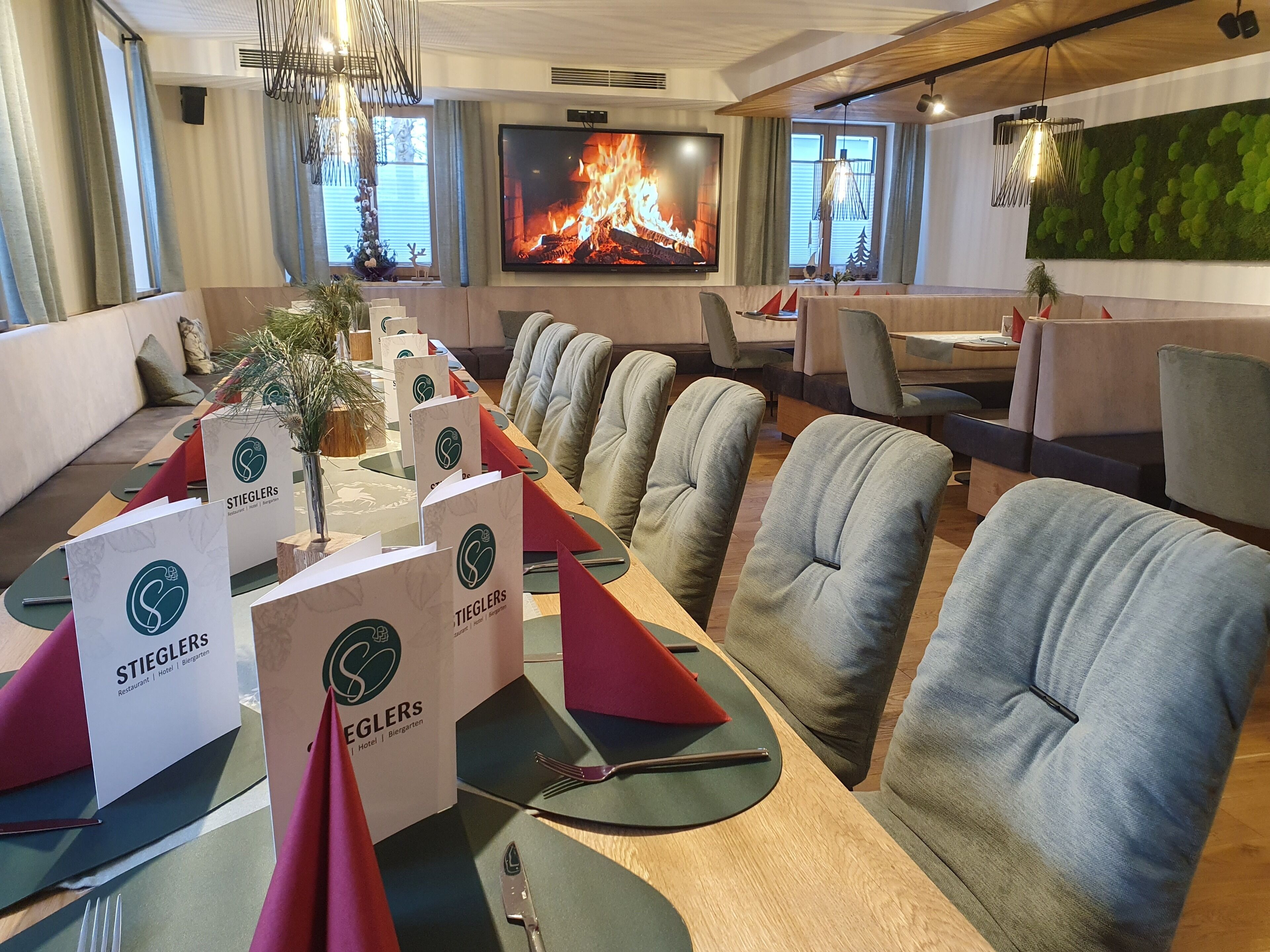 A conference room with a long table, multiple chairs, and a large TV screen displaying a fireplace.